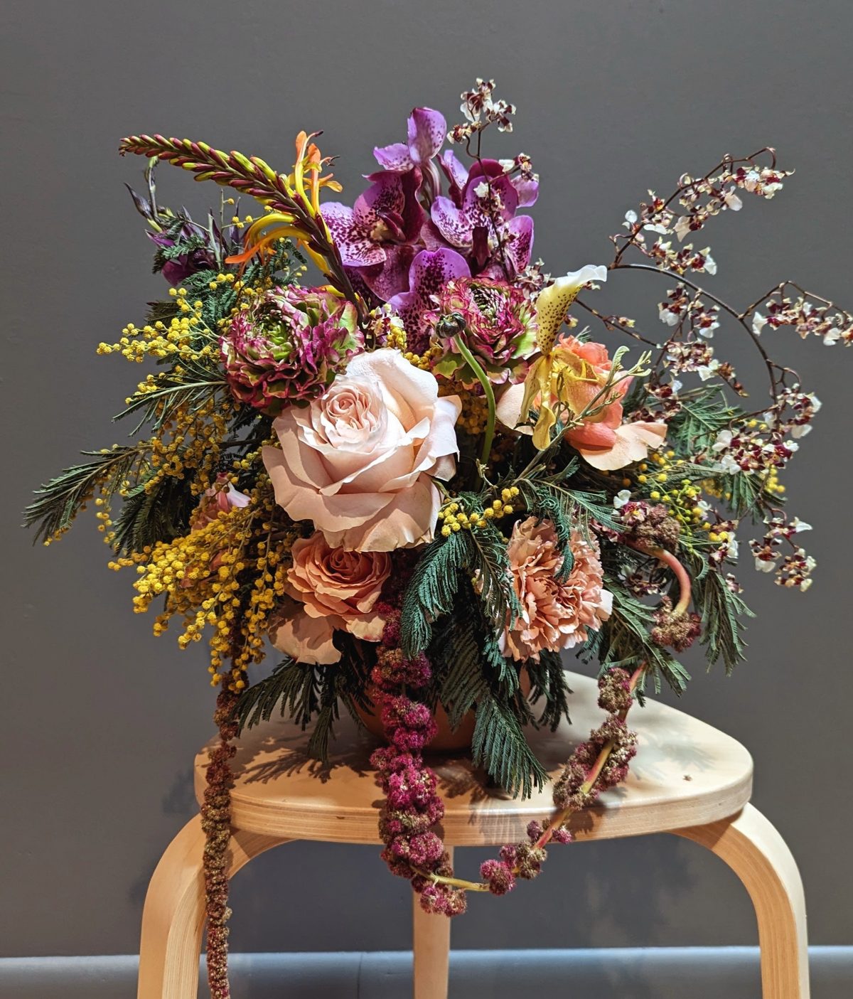 Arrangement of roses, orchids and mimosa on a stool